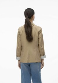 Beige blazer with a tailored fit, featuring a notched collar and white pleated cuffs, paired with light blue wide-leg jeans.