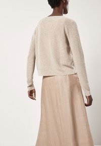 Maglione color beige chiaro e scintillante con una vestibilità rilassata e maniche lunghe, abbinato a una gonna beige fluente, visto da dietro.