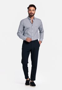 Geverfde blauw en witte overhemden met lange mouwen, gecombineerd met een donkere broek en zwarte instap schoenen. Eenvoudig design en een getailleerde pasvorm.