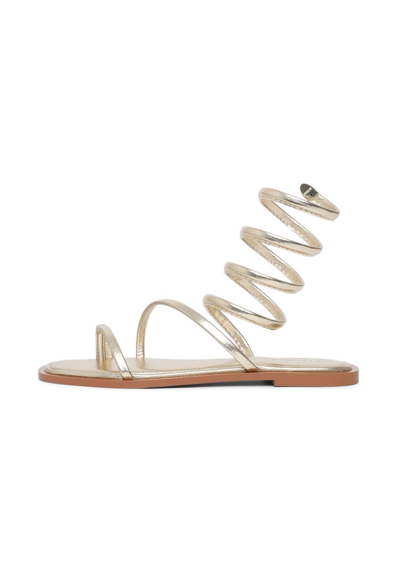 Gold metallic heeled sandals with a spiral strap design and flat sole. Features thin, minimalistic straps for a sleek appearance.