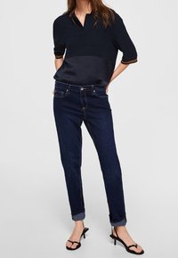Polo bleu foncé à manches courtes avec un panneau avant en satin, associé à un jean denim foncé avec des revers roulés et un design minimaliste.