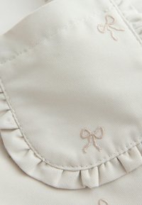 Helebeež kangas voldilise kraega, millel on pehmed helepunased tikitud vibu. Sile tekstuur peene soonikuga detailiga.