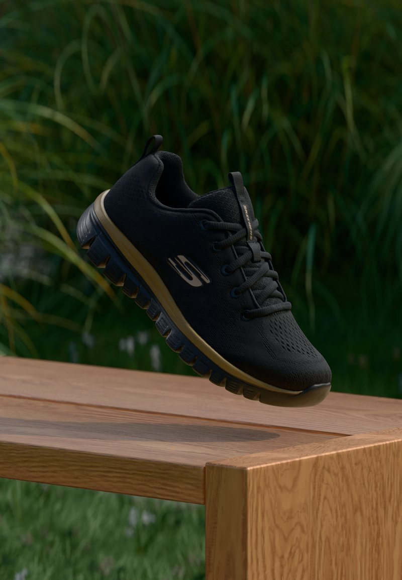 Schwarzer Sportschuh mit strukturiertem Mesh-Obermaterial, Schnürsenkeln und gepolsterter Sohle. Mit einem goldenen Akzent entlang der Sohle und einem Seitenlogo.