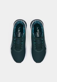 Ζευγάρι σκούρα πράσινα αθλητικά παπούτσια Puma με μαύρα κορδόνια και λευκές σόλες, σε θέαση από πάνω σε λευκό φόντο.