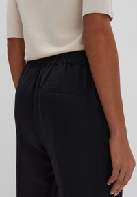 Zwarte joggingbroek met een elastische tailleband, met een gladde textuur en een achterzak. Het materiaal lijkt lichtgewicht en ademend te zijn.