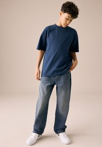 Tamnoplava majica kratkih rukava, opuštenog kroja, u kombinaciji sa svijetloplavim širokim trapericama i bijelim tenisicama sa srebrnim detaljima.