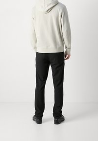 Světlounce šedá mikina s kapucí na stahovací šňůrku, doplněná o černé kalhoty a černé boty. Hladká textura látky, základní design bez vzorů.