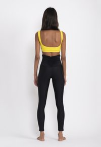 Yellow sports bra with wide straps paired with high-waisted black leggings featuring gathered texture at the waist.
