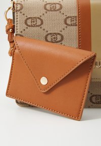 Brown leather cardholder features a triangular flap with a snap closure, displayed next to a patterned tan bag with a gold accent.