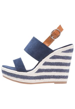 Granatowy zamszowy sandał na koturnie z dwoma paskami na cholewce, brązowym skórzanym paskiem na kostkę oraz plecioną, paskowaną podeszwą espadrylową w kolorze niebieskim i białym.