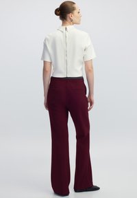 Witte korte mouwen top met een kraag en een ritssluiting aan de achterkant, gecombineerd met hooggetailleerde bordeauxrode broek met zijzakken en een rechte pasvorm.