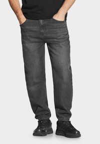 Ciemnoszare dżinsy o luźnym kroju, z tradycyjnymi kieszeniami i gładką teksturą, w połączeniu z czarnymi butami sportowymi.