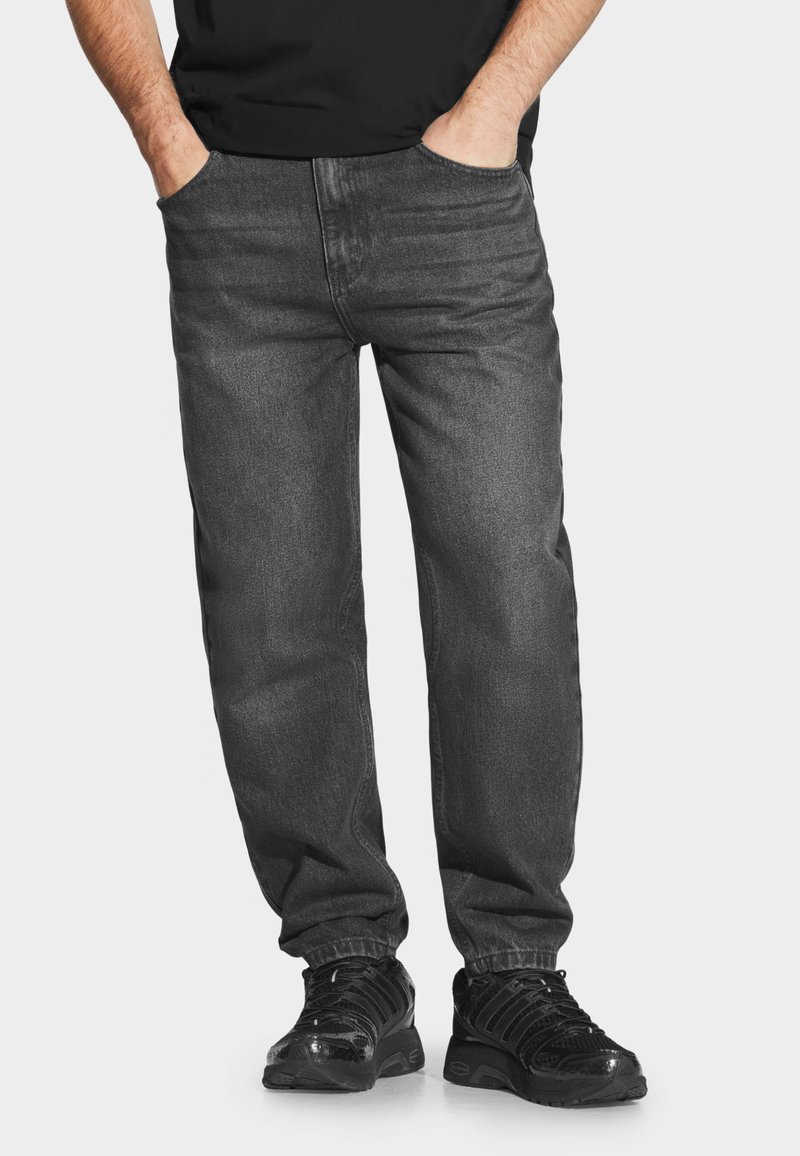 Ciemnoszare dżinsy o luźnym kroju, z tradycyjnymi kieszeniami i gładką teksturą, w połączeniu z czarnymi butami sportowymi.