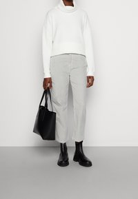 Weißer gerippter Rollkragenpullover, hellgraue Cordhosen, schwarze Leder-Stiefeletten und eine schwarze Tote-Tasche. Einfaches und modernes Design.