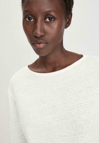 Weißer leichter Sweatshirt mit strukturiertem Finish, mit weitem Ausschnitt und subtilen Nähdetails, getragen von einem Model vor neutralem Hintergrund.