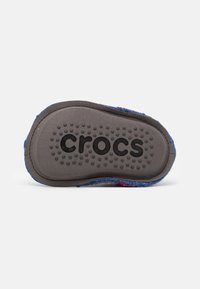 Scarpa slip-on Crocs con suola in gomma grigia, caratterizzata da punti testurizzati per una migliore aderenza e una tomaia blu con motivo multicolore. Logo visibile sulla suola.