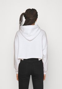 Sudadera recortada en suave tejido blanco con capucha, con hombros caídos y puños acanalados, combinada con jeans negros de cintura alta.