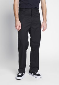 Pantalones negros de tela, con un diseño de pierna recta, presillas para cinturón y un frente limpio. Combinados con zapatillas negras.