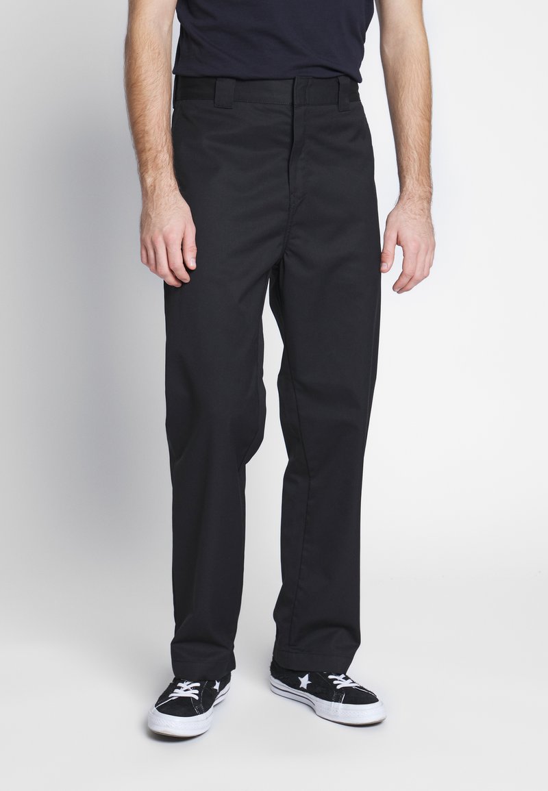 Pantalones negros de tela, con un diseño de pierna recta, presillas para cinturón y un frente limpio. Combinados con zapatillas negras.