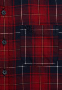 Rood en marineblauw geruit overhemd met knoopsluiting, beschikt over een borstzak, zwarte knopen en witte accenten in het patroon. Zacht textiel.