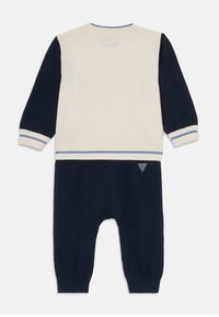 Strikket romper i krem og marineblå. Lange ermer, ribbede mansjetter og en liten logo-detalj. Myk tekstur og kontrastfargede ermer.