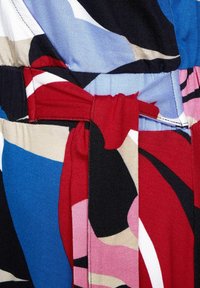 Gros plan d'une ceinture en tissu nouée sur un vêtement à motifs abstraits multicolores avec des formes rouges, bleues, noires, roses et beige.