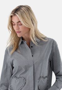 Button-up shirt in black and white gingham pattern, featuring textured heart-shaped pockets and a classic collar.