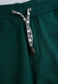 Zielone dresowe spodnie z bawełny z prążkowanym pasem i sznurkiem, z napisem "COLLEGE" w kolorze czarnym. Posiadają szczegóły bocznej kieszeni.