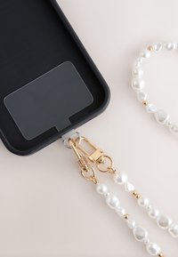 Black phone case attached to a white and gold pearl beaded strap with gold clasps on a light surface.