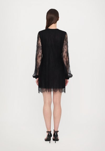 Rochie neagră din dantelă cu mâneci lungi și transparente, cu un corset ajustat și un tiv evazat. Prezintă detalii intricate din dantelă la margini, asortată cu pantofi cu toc negri.
