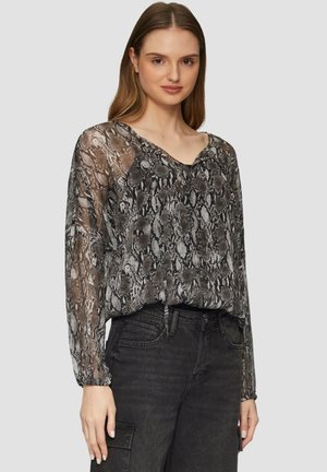Blouse en imprimé serpent noir et gris, en voile, avec des manches longues, un décolleté en V et des poignets froncés, associée à un jean foncé.