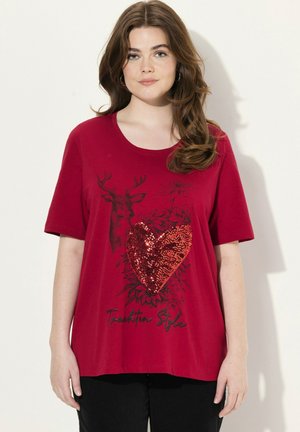 T-shirt rouge à manches courtes avec un graphique de cerf noir et un design de cœur en sequins. Tissu doux avec une coupe décontractée, accompagné de texte.