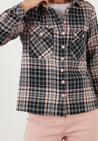 Camicia a quadri nei toni del nero, blu e rosa, con due tasche sul petto e bottoni rosa. Realizzata in tessuto testurizzato, progettata con maniche lunghe.