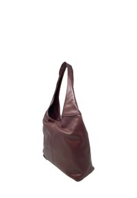 Brązowa skórzana torba na ramię o miękkiej teksturze, wydłużonym kształcie i szerokim otwarciu. Posiada jeden, zakrzywiony pasek do noszenia.