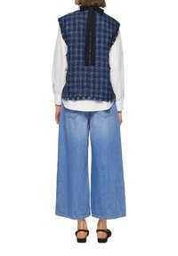 Blauer Tweed-Wester mit Rüschenkanten und schwarzem Band auf der Rückseite, kombiniert mit weit geschnittenen hellblauen Jeans und schwarzen Sandalen.