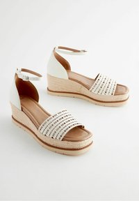 Sandalias de cuña con una correa de tobillo de cuero blanco, plantilla de color beige y correa blanca perforada. Cuña envuelta en yute y suela de goma.