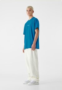 Blå kortærmet t-shirt med rund halsudskæring, parret med hvide, løstsiddende bukser af tekstureret stof. Hvide sneakers fuldender looket.