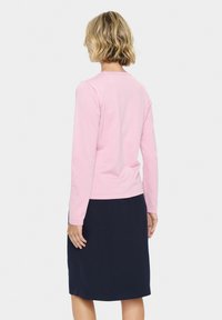 Svetlo roza dolgi rokav z okroglim izrezom, v kombinaciji s temno mornarsko krilo do kolen. Gladka tekstura, prilegan dizajn, minimalno okrasje.