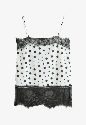 Balts krekliņš ar melniem polka punktiem, melnu mežģīņu apdari pie kakla un apakšmalas, un plānas polka punktu plecu siksnas.