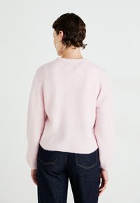 Απαλή ροζ, φούξια ζακέτα με μακριά μανίκια και στρογγυλή λαιμόκοψη, συνδυασμένη με σκούρα τζιν παντελόνια που διαθέτουν αντίθετες ραφές.