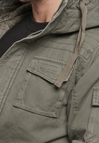 Oliwkowo-zielona kurtka z kapturem i zamkiem błyskawicznym, posiada duże przednie kieszenie oraz teksturowaną tkanin�ę. Regulowany sznurek w kapturze.