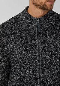 Cardigan a maglia con zip in grigio scuro e nero. Presenta un colletto alto, un motivo testurizzato e una zip frontale con un tirante in plastica.