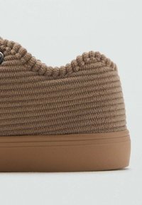 Sneaker marrone con texture, dotato di una tomaia in tessuto a coste e suola in gomma liscia. Presenta un bordo superiore arrotondato e non ha lacci o accessori visibili.
