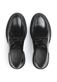 Scarpe in pelle nera con una finitura liscia, punta arrotondata, design con lacci e suola in gomma nera a contrasto. Presentano dettagli di cucitura visibili.