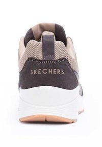 Baskets Skechers avec une tige en mesh beige, un panneau en suède gris foncé, un col rembourré et une semelle blanche avec une semelle extérieure en caoutchouc texturé.