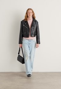 Black leather cropped moto jacket with silver zippers, paired with a light pink sweater and light blue wide-leg jeans. Model holds a black bag.