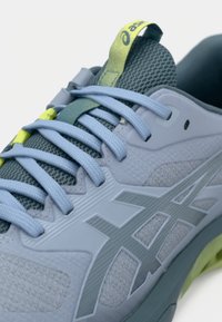 Ανοιχτό μπλε αθλητικό παπούτσι με πλέγμα και συνθετικά υλικά, επίπεδες κορδόνες και υφή επιφάνειας, με πράσινες και κίτρινες λεπτομέρειες.