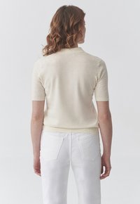 Maglione crema a maniche corte realizzato in materiale leggero, con scollatura rotonda e dettagli a coste all'orlo e alle maniche.