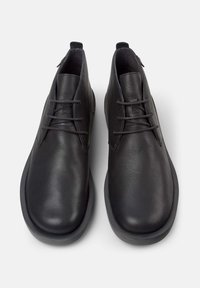 Bottines en cuir noir avec un bout arrondi, texture lisse, coutures subtiles et lacets fins. Dotées d'une semelle en caoutchouc basse.