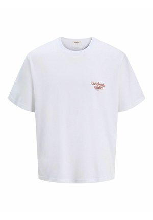 Chlapec sa usmieva, nosí biele tričko s nápisom "Originals Studio", rifľové šortky, biele ponožky a čierno-biele tenisky, stojí na bielom pozadí.